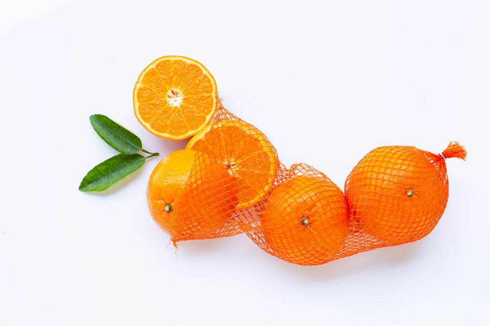 High vitamin C. Orange in net bag with ripe half of orange on white background