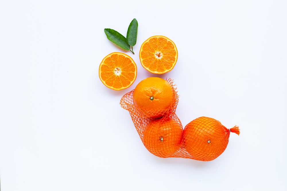 High vitamin C. Orange in net bag with ripe half of orange on white background