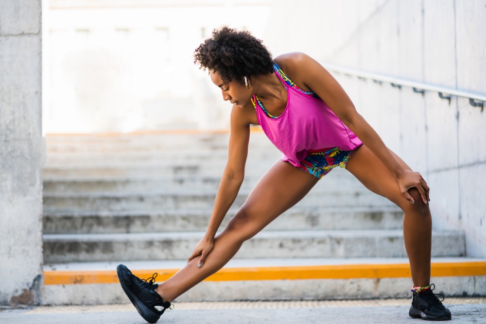 Portrait of afro athlete woman stretching legs before exercise outdoors. Sport and healthy lifestyle.. Afro athlete woman stretching legs before exercise.