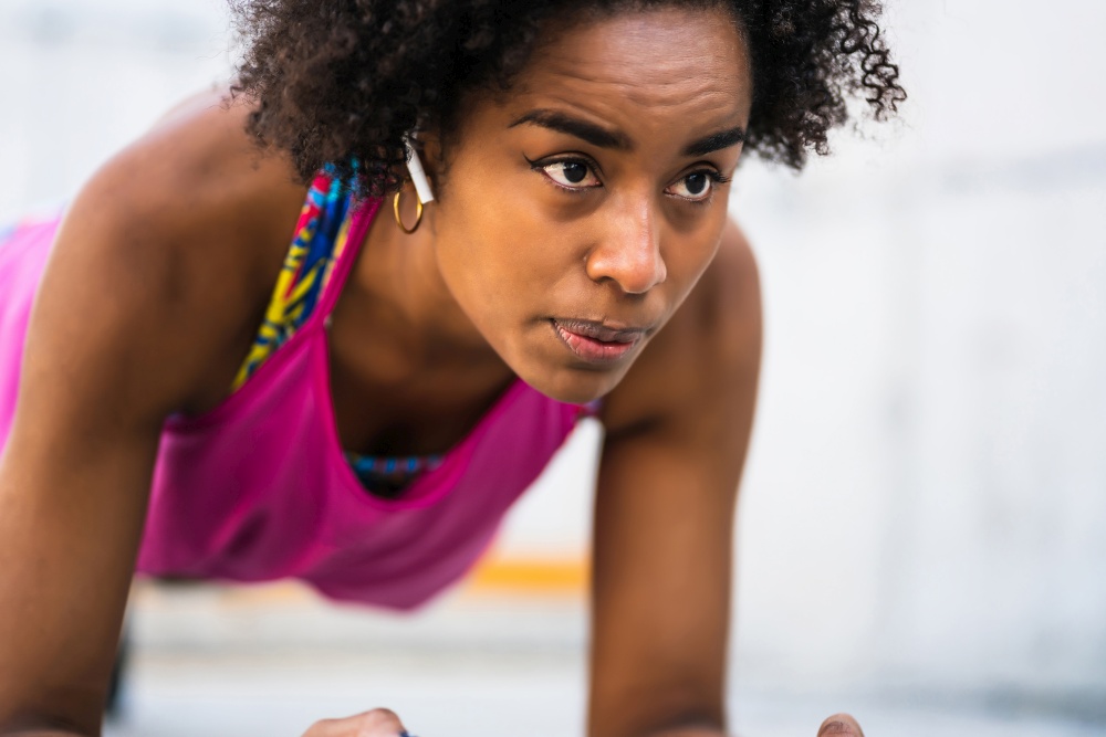 Portrait of afro athlete woman doing pushups on floor outdoors. Sport and healthy lifestyle concept.. Afro athlete woman doing pushups outdoors.
