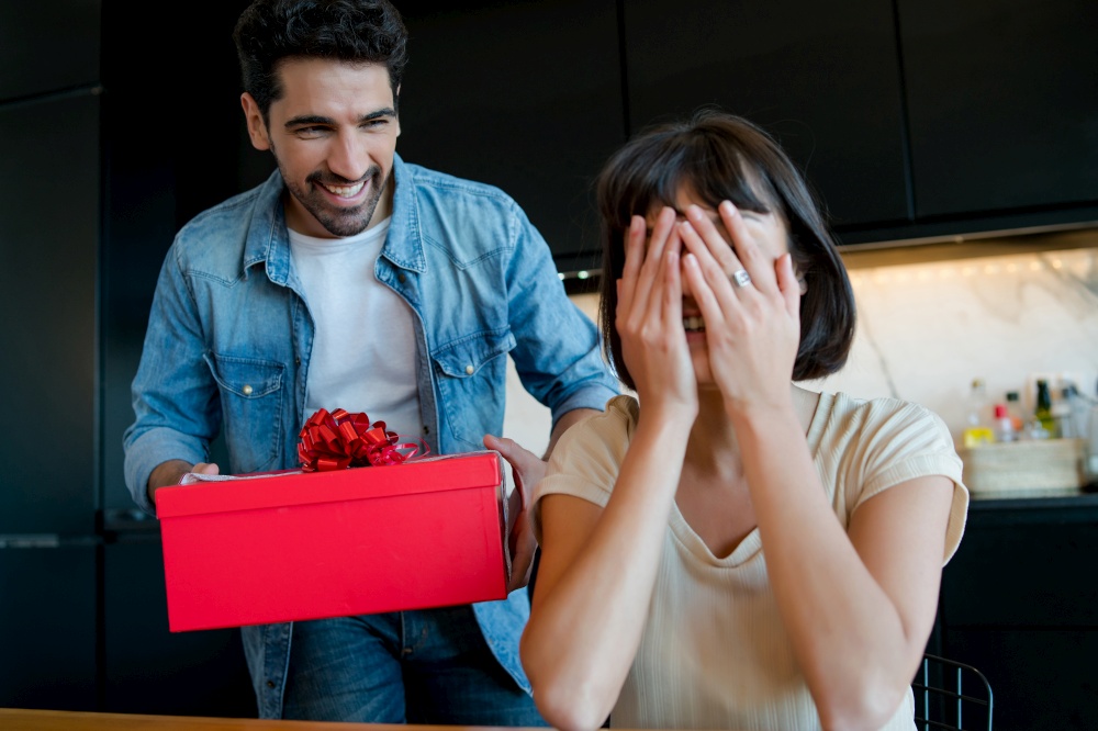Portrait of young man surprising his girlfriend with a gift box. Celebration and valentine&rsquo;s day concept.. Man surprising his girlfriend with a gift.