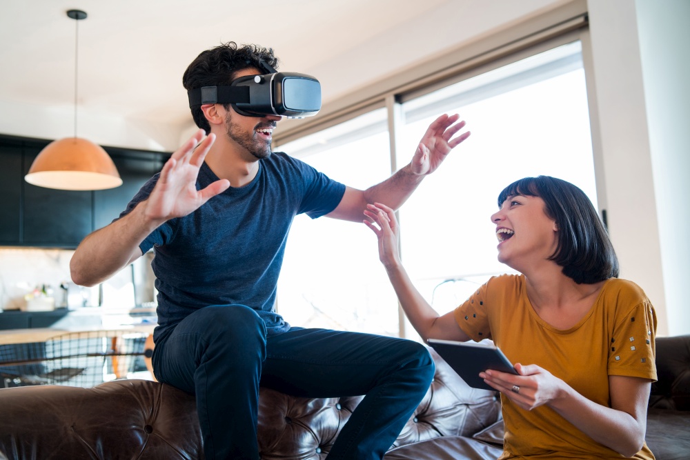 Portrait of young couple having fun together and playing video games with VR glasses while staying at home. New normal lifestyle concept.