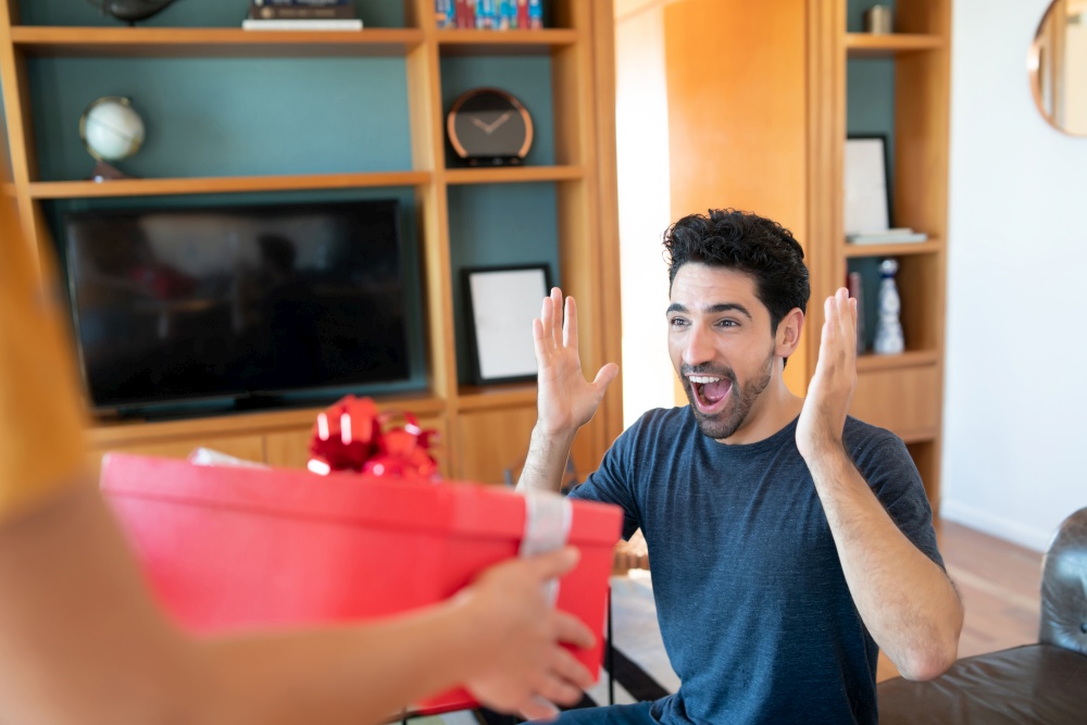 Portrait of a woman surprising her boyfriend with a present. Celebration and valentine&rsquo;s day concept.