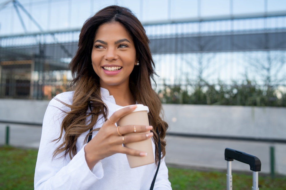 Portrait of young traveler woman holding a cup of coffee while sitting outdoors on the street. Urban concept. Tourism concept.