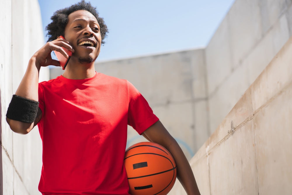 Portrait of afro athlete man talking on the phone and relaxing after training outdoors. Sport and healthy lifestyle.