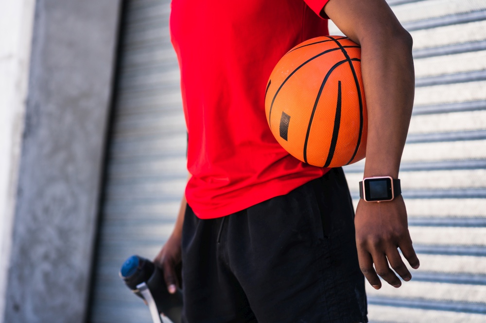 Portrait of afro athlete man holding a basketball ball while standing outdoors. Sport and healthy lifestyle.