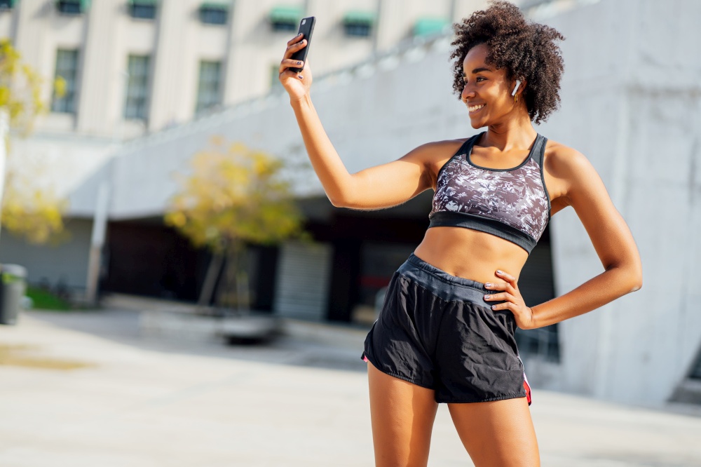 Afro athletic woman taking a selfie with her mobile phone and relaxing after work out outdoors. Sport and healthy lifestyle.