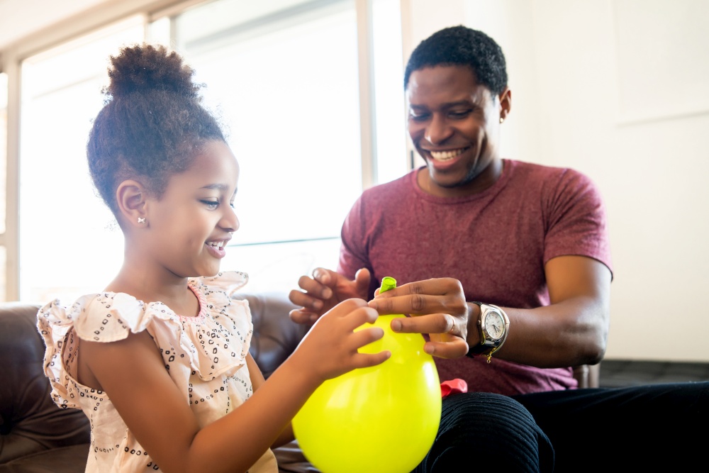 Portrait of a daughter and father having fun together and playing with balloons at home. Monoparental concept.