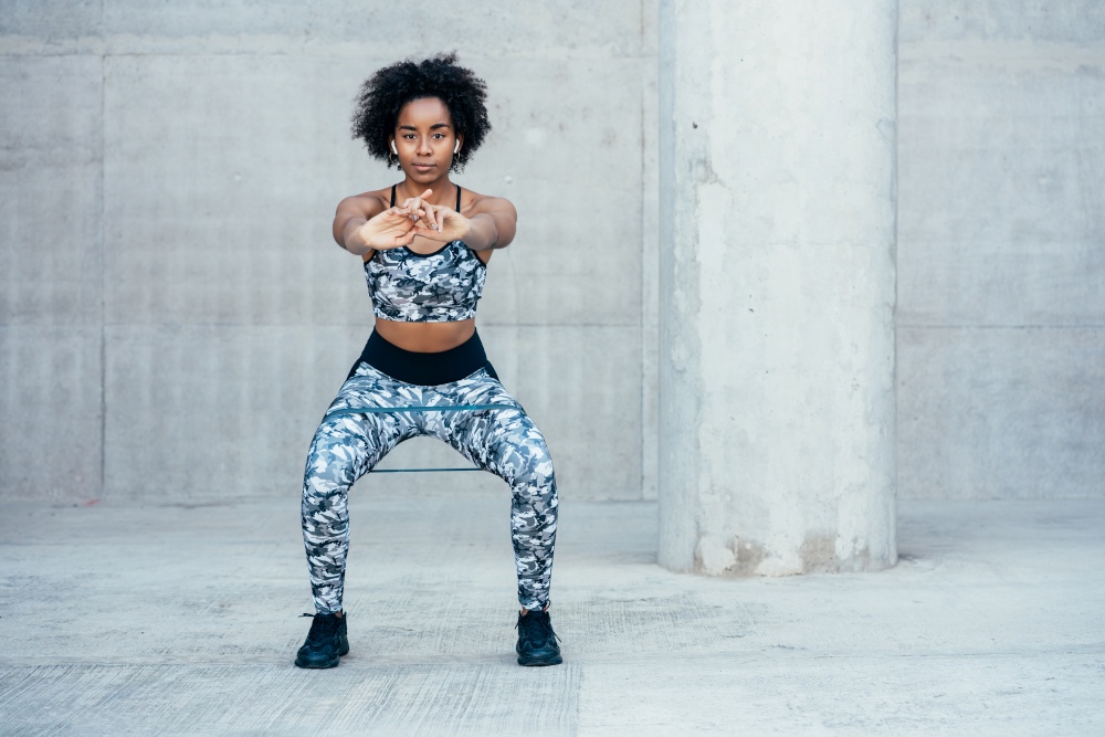 Afro athletic woman exercising and doing squat leg outdoors. Sport and healthy lifestyle concept.