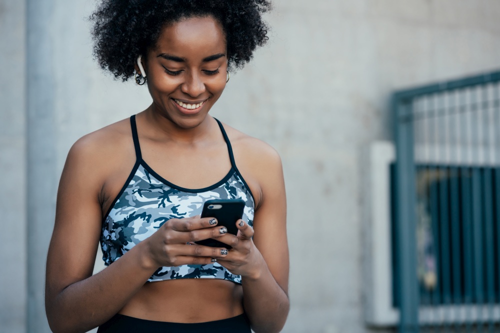 Afro athletic woman using her mobile phone and relaxing after work out outdoors. Sports and technology concept.