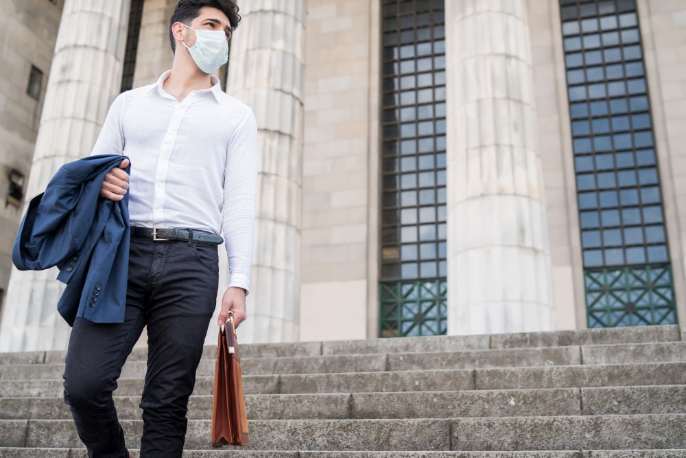 Businessman wearing a face mask and holding a briefcase while walking to work outdoors. New normal lifestyle. Business concept.