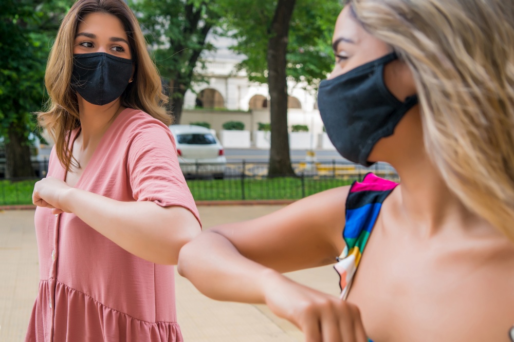 Portrait of two young friends wearing face mask and bumping elbows outdoors. New normal lifestyle concept.