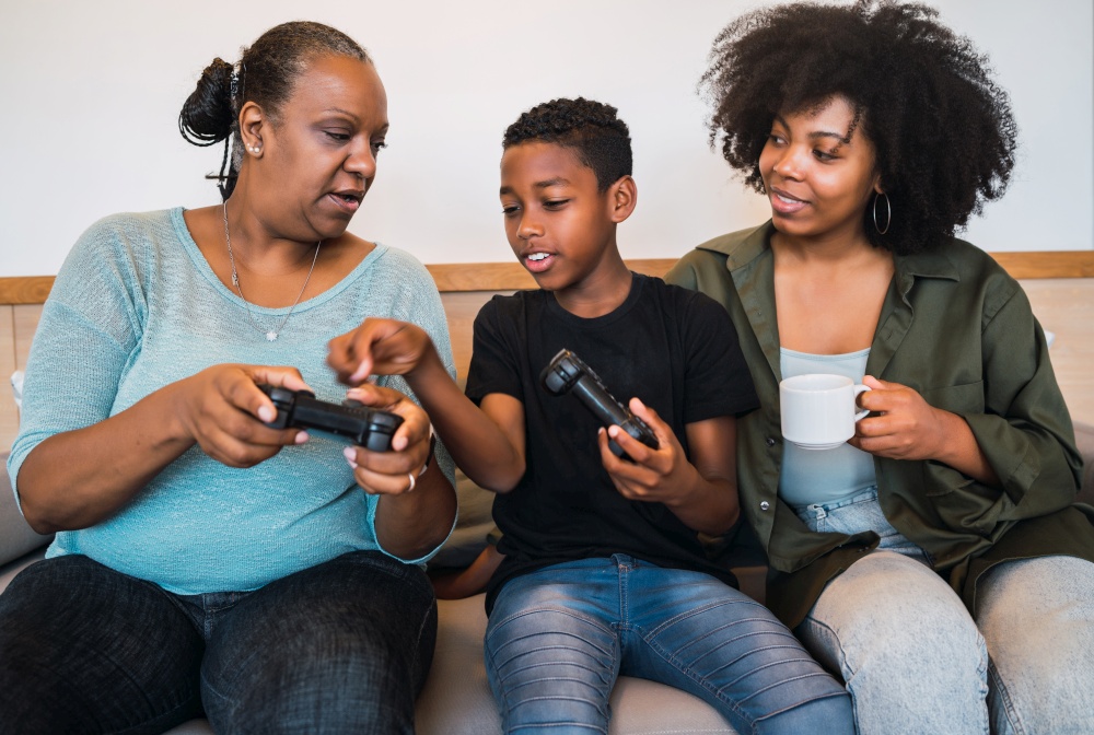 Portrait of African American child teaching grandmother and mother how to use joystick to play video games. Technology and lifestyle concept.