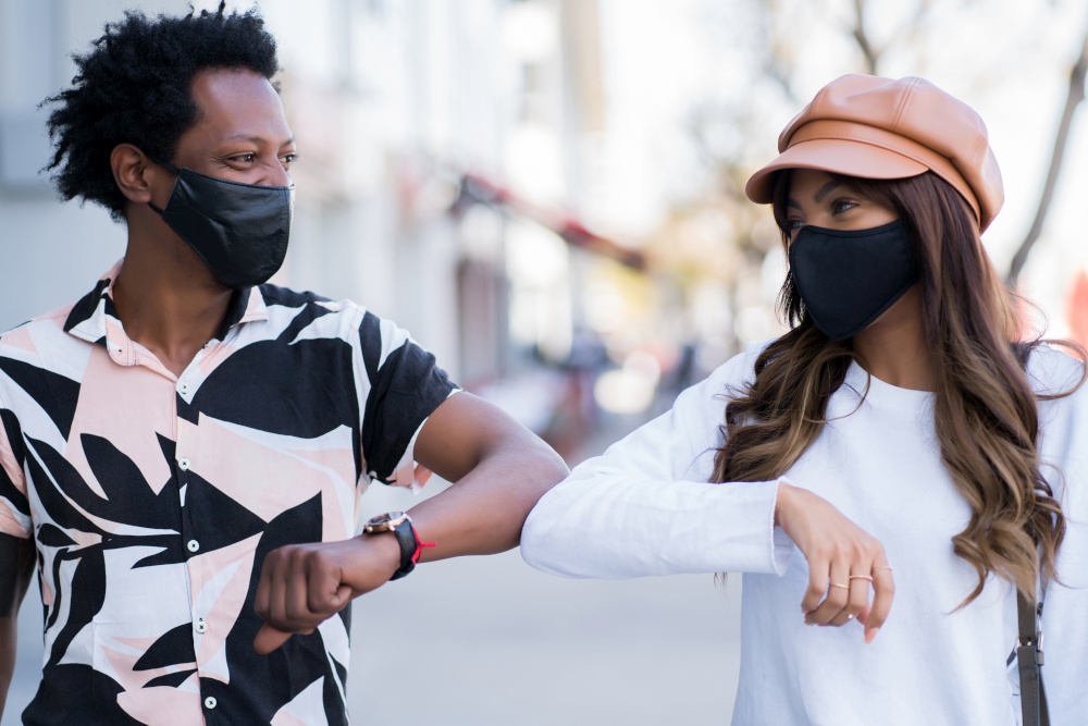 Portrait of young couple wearing face mask and tapping each other with their elbows to say hello while standing outdoors. New normal lifestyle concept.