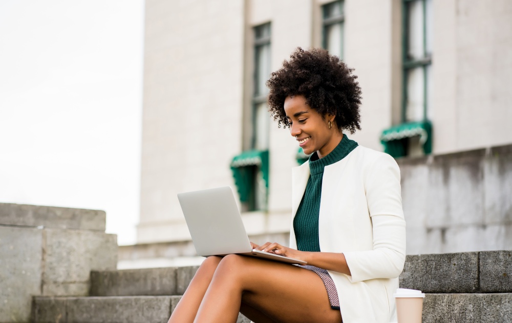 Afro business woman using her laptop while sitting on stairs outdoors. Urban and business concept.