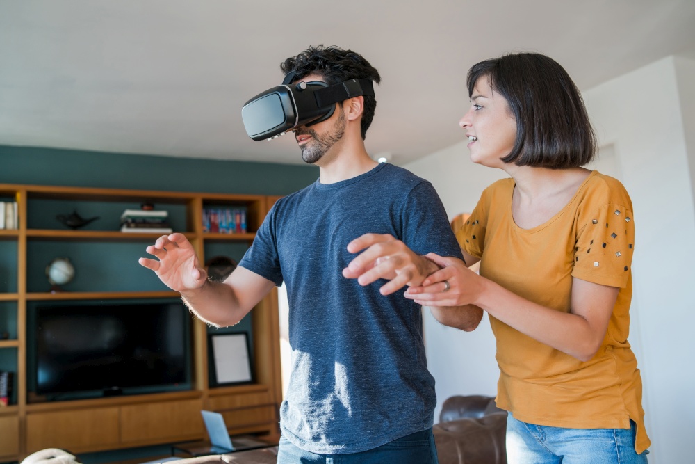 Portrait of young couple having fun together and playing video games with VR glasses while staying at home. New normal lifestyle concept.