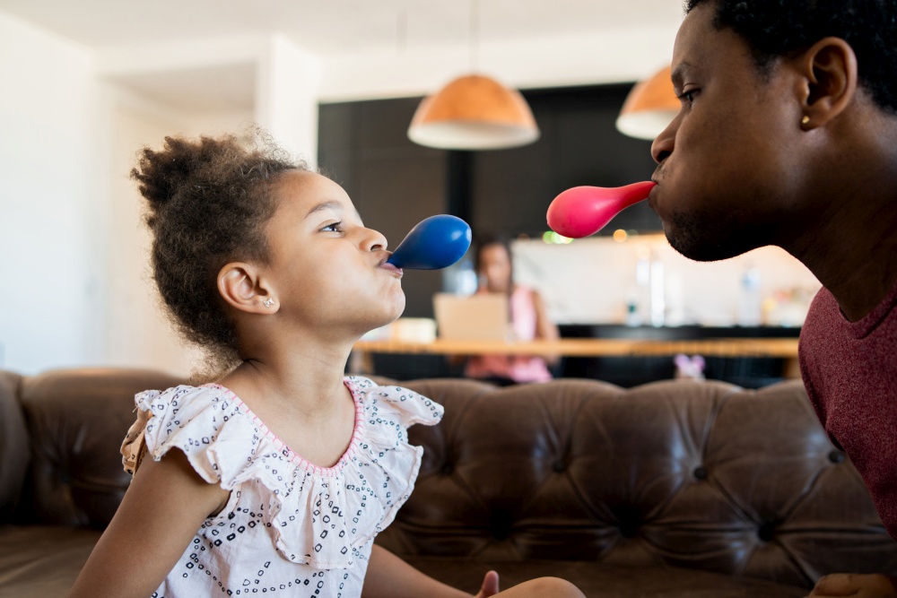 Portrait of a daughter and father having fun together and playing with balloons while staying at home. Monoparental concept.