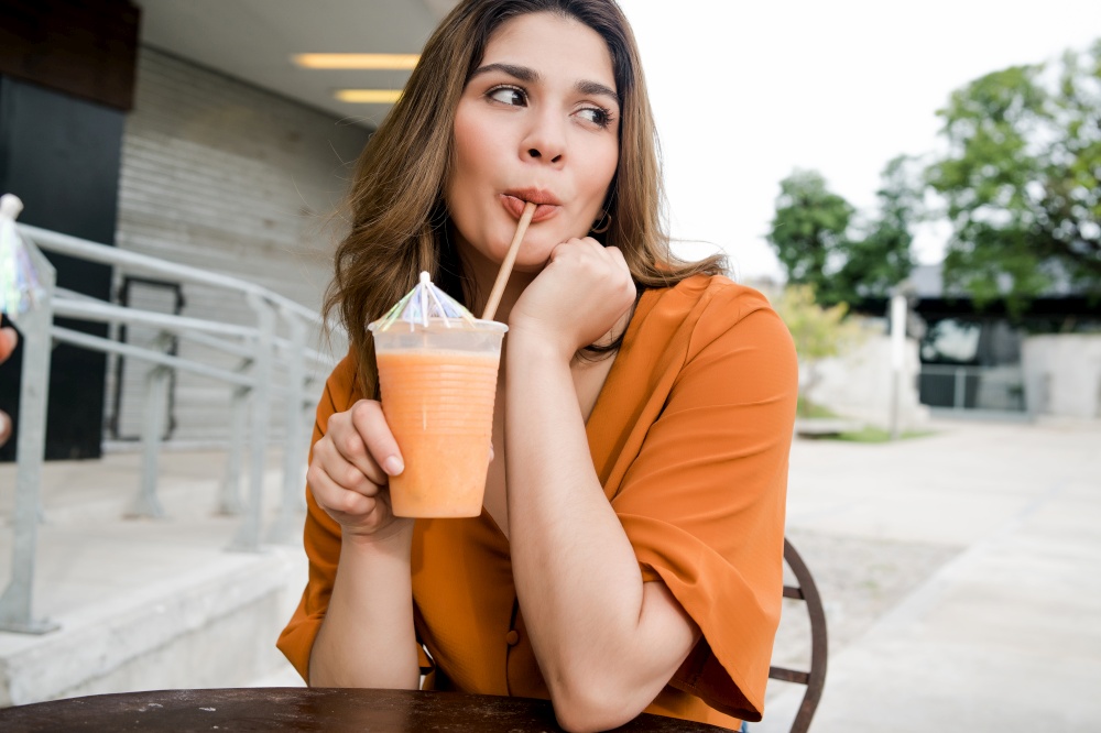 Portrait of young woman drinking a fresh juice fruit at a coffee shop outdoors. Urban concept.