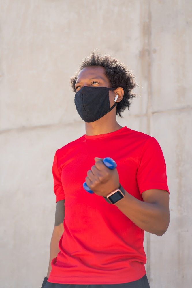 Afro athletic man wearing face mask and doing exercise with dumbbell outdoors. New normal lifestyle. Sport and healthy lifestyle concept.