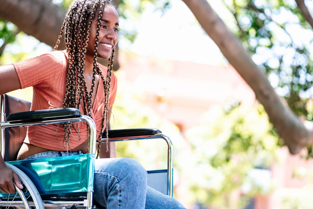 African American woman in a wheelchair smiling and looking at the camera while in the park.