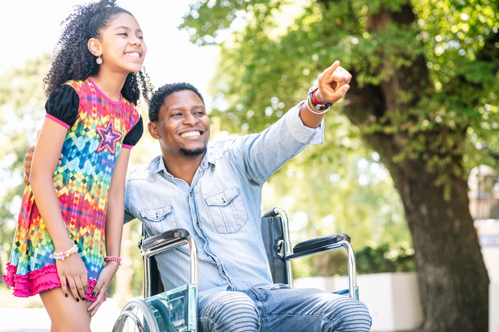 An african american man in a wheelchair enjoying a walk outdoors with his daughter.