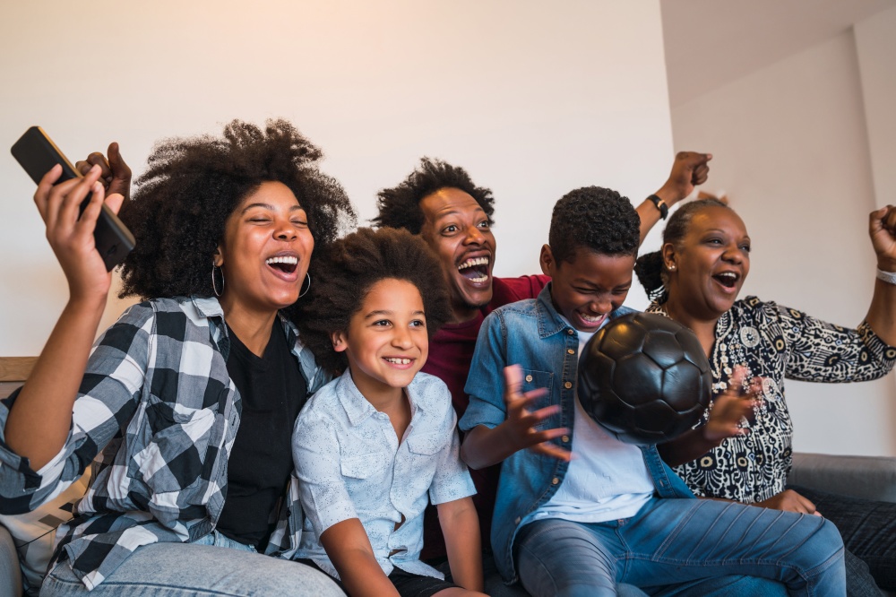 Happy african american multi-generation family watching soccer match on television in living room at home. Family and sport concept.