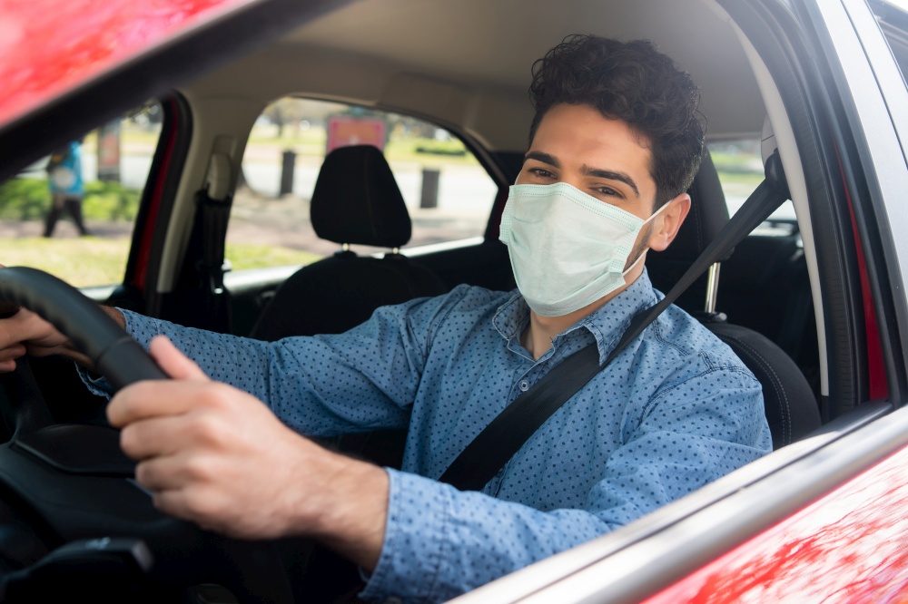 Portrait of young man using face mask while driving his car on his way to work. Transport concept. New normal lifestyle concept.