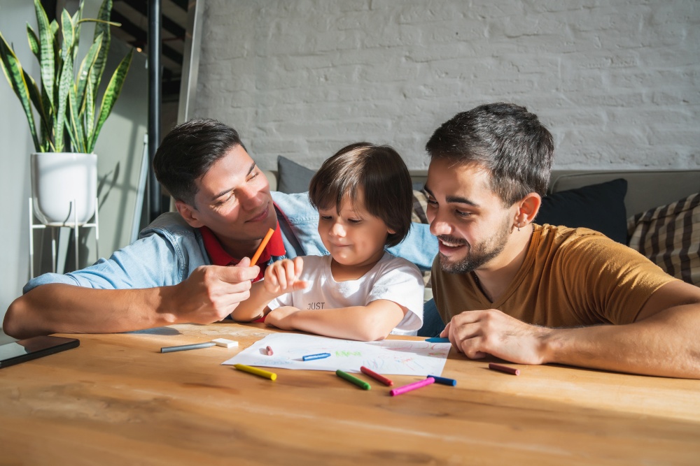 Gay couple and their son having fun together while drawing something on a paper at home. Family concept.