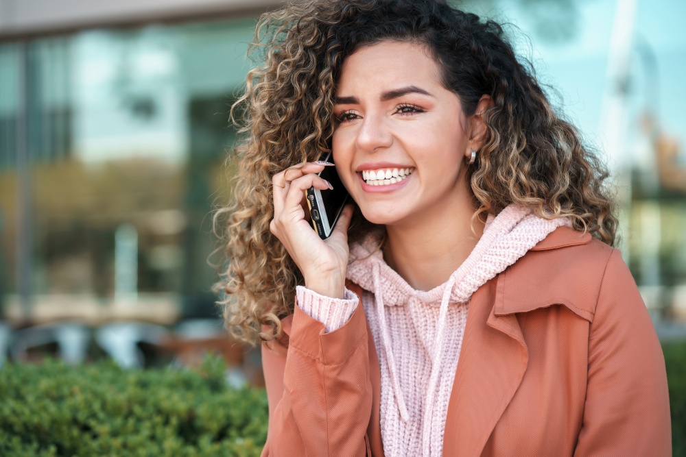 Young latin woman smiling while talking on the phone outdoors in the street. Urban concept.