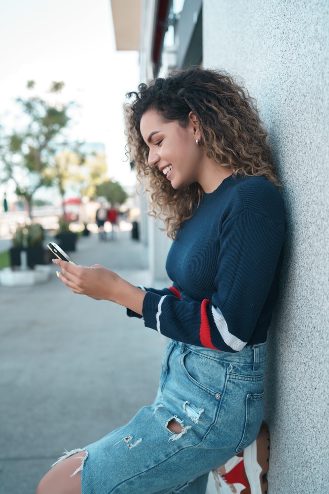Young woman using her mobile phone while standing outdoors on the street. Urban concept.