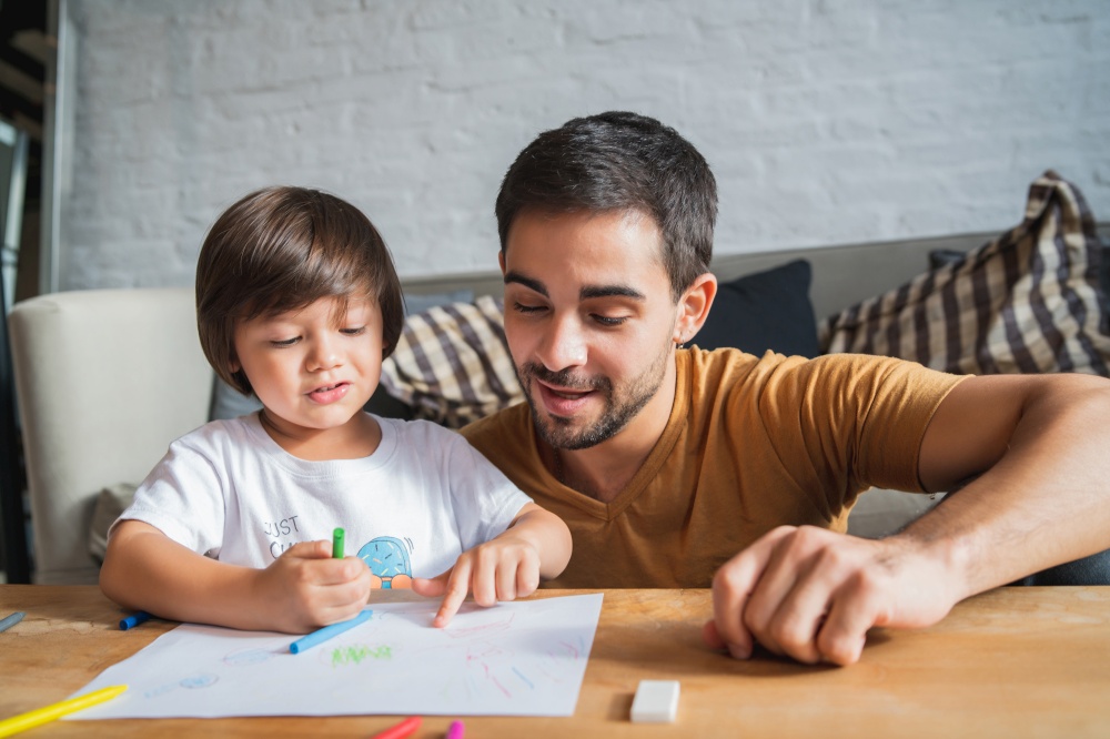 Little boy and his father spending time together drawing at home.
