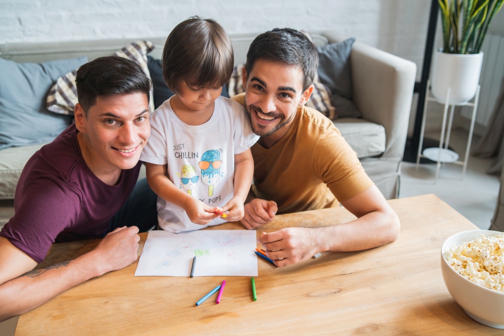 Gay couple having fun with their son while drawing something on a paper at home. Family concept.