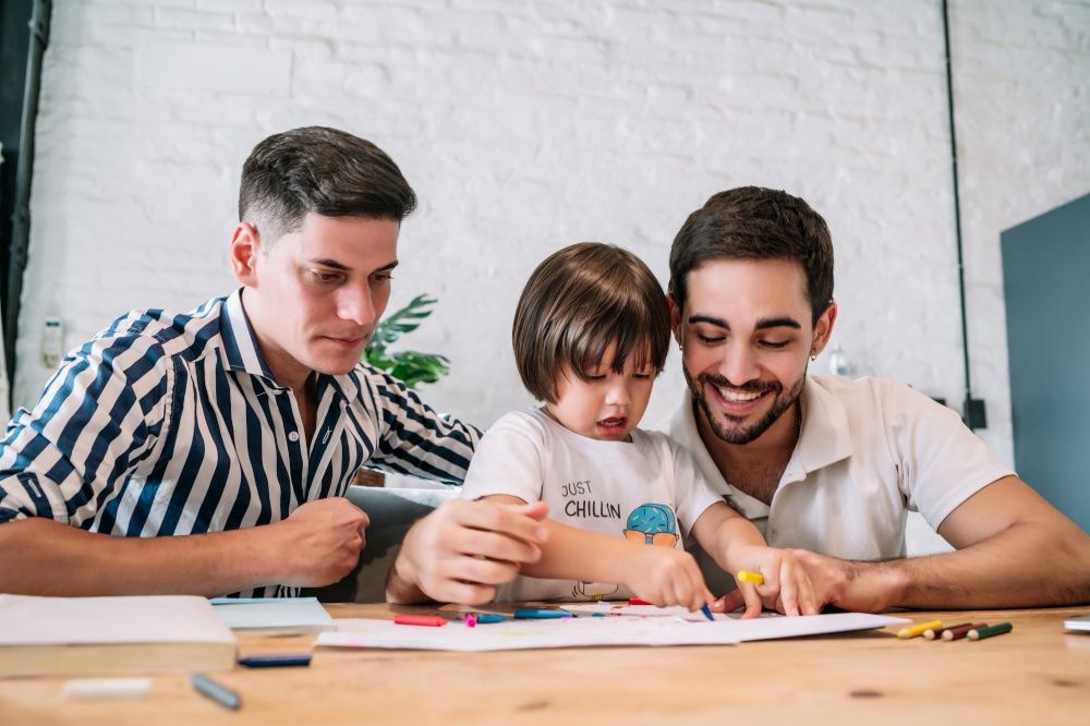 Gay couple having fun with their son while drawing something on a paper at home. Family concept.