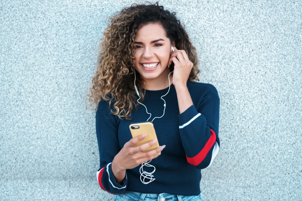 Young latin woman smiling while using her mobile phone outdoors at the street. Urban concept.