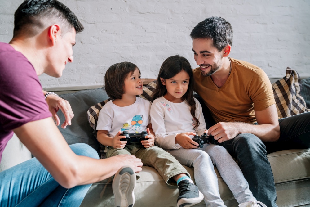 Gay couple having fun while playing video games with their kids at home. Family concept.