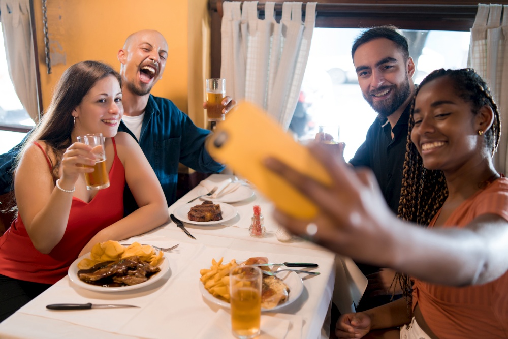 Group of diverse friends taking a selfie with a mobile phone while enjoying a meal together in a restaurant. Friends concept.