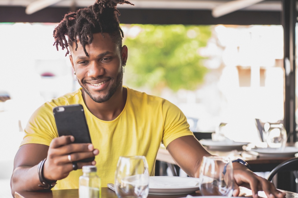 African american man using his mobile phone while sitting in a restaurant.
