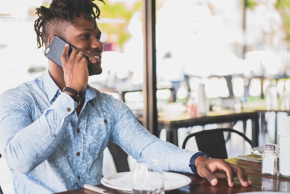 Young african american man talking on the phone while sitting in a restaurant.
