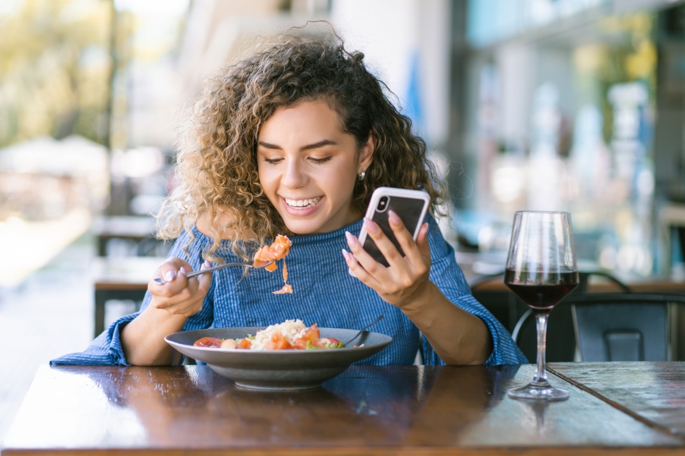 Young woman using a mobile phone while having lunch at a restaurant.