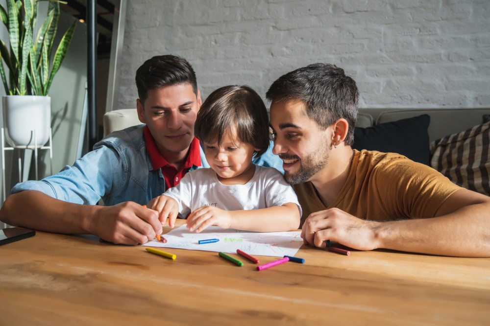 Gay couple having fun with their son while drawing together at home. Family concept.