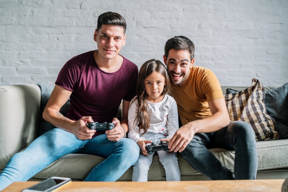 Gay couple having fun while playing video games with their daughter at home. Family concept.