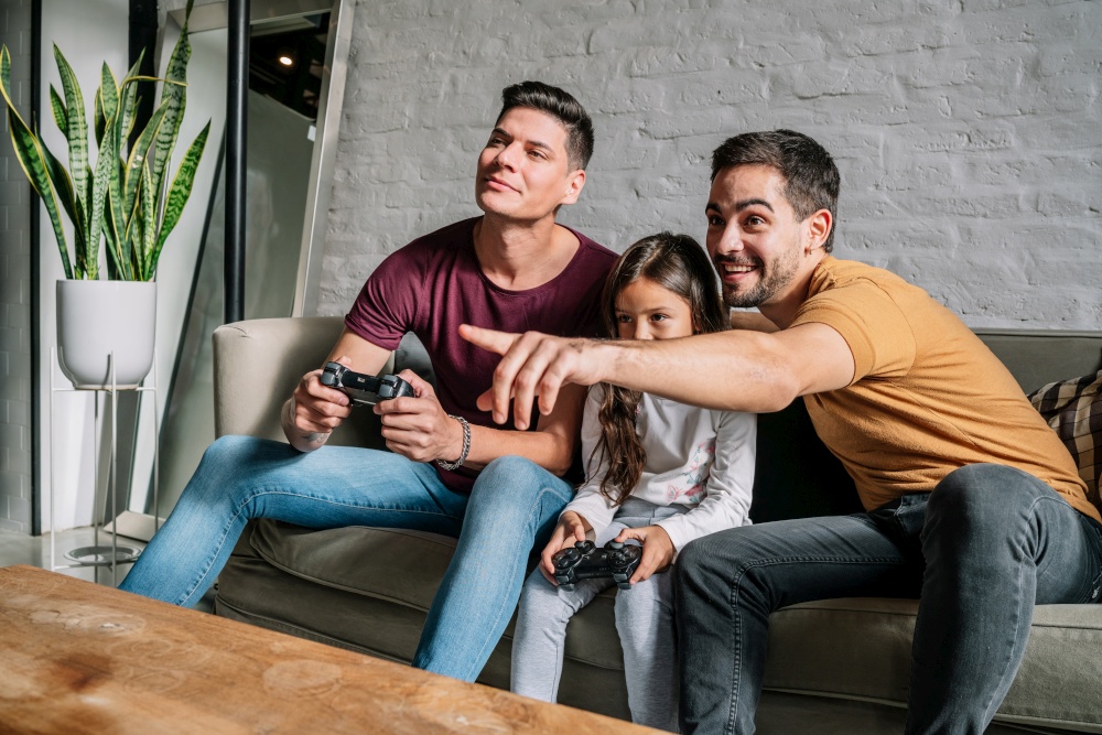 Gay couple having fun while playing video games with their daughter at home. Family concept.