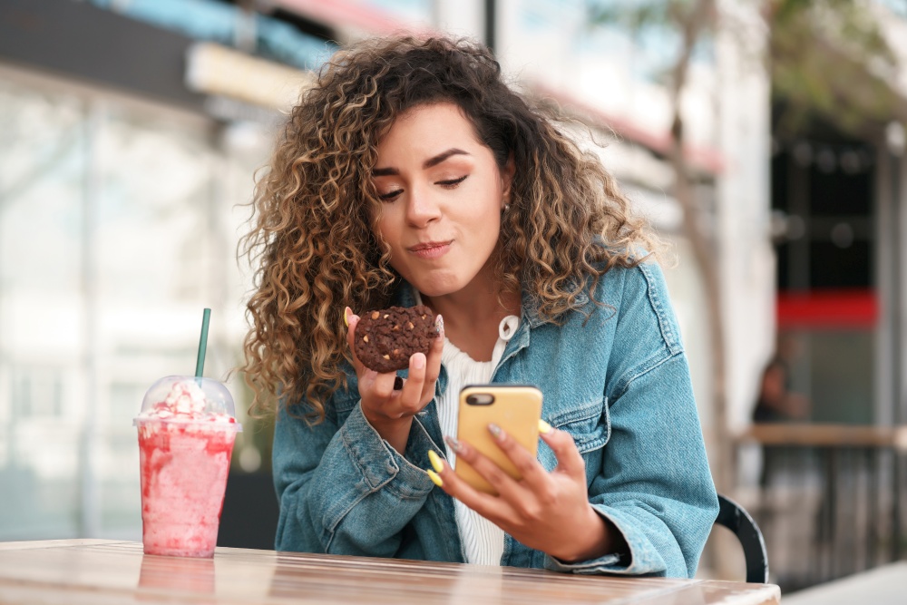 Latin young woman using her mobile phone while sitting at a coffee shop outdoors on the street. Urban concept.