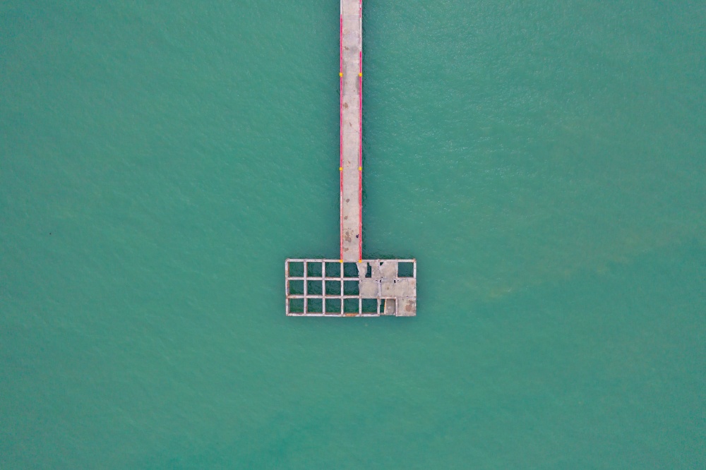Aerial view of old marina port or pier in harbor in island, ocean or bay with blue turquoise seawater in travel trip and transportation concept. Top view.
