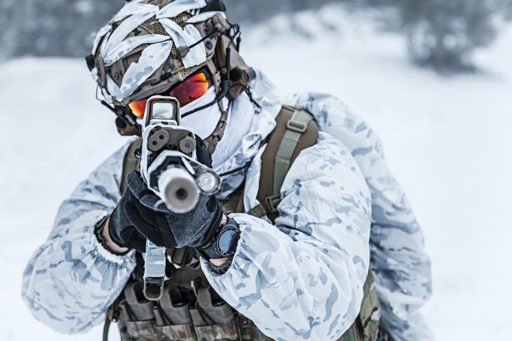 Winter arctic mountains warfare. Action in cold conditions. Trooper with weapons in forest somewhere above the Arctic Circle, pointing at camera. Winter arctic warfare