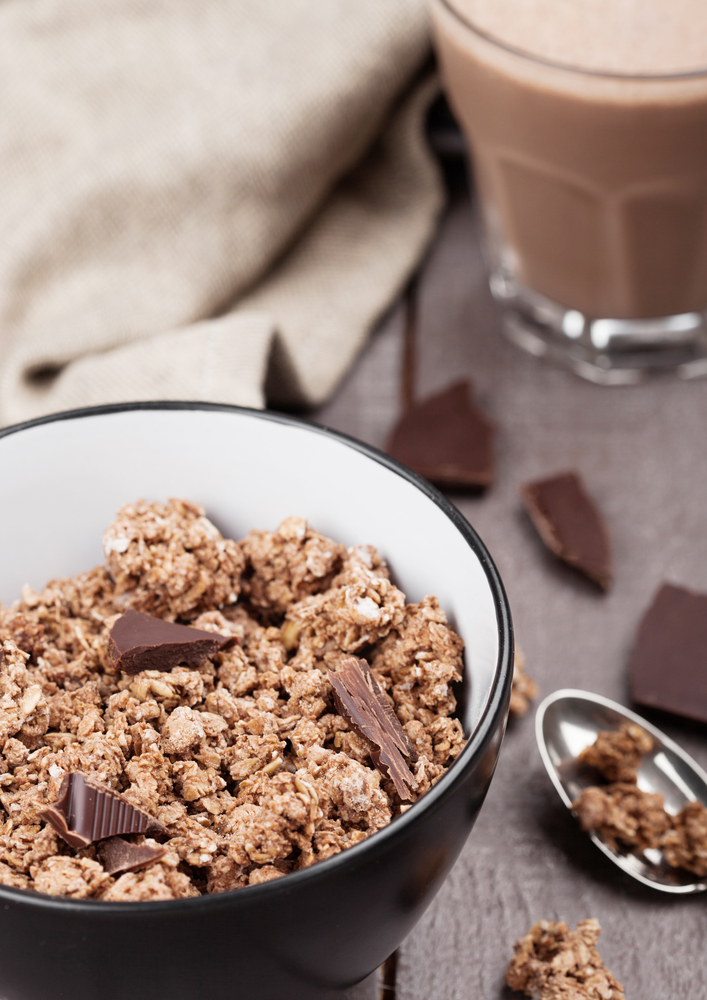 Bowl with organic chocolate granola breakfast cereal on wooden background with chocolate bar on wooden background