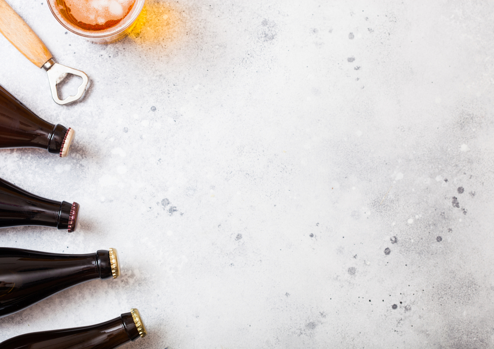 Glass bottles of craft lager beer with raw wheat and opener on stone kitchen table background.