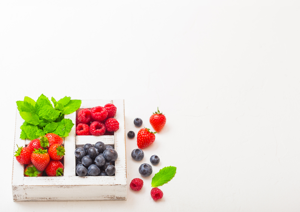 Fresh raw organic berries  in white wooden box on kitchen table background. Space for text. Strawberry, Raspberry, Blueberry and Mint leaf