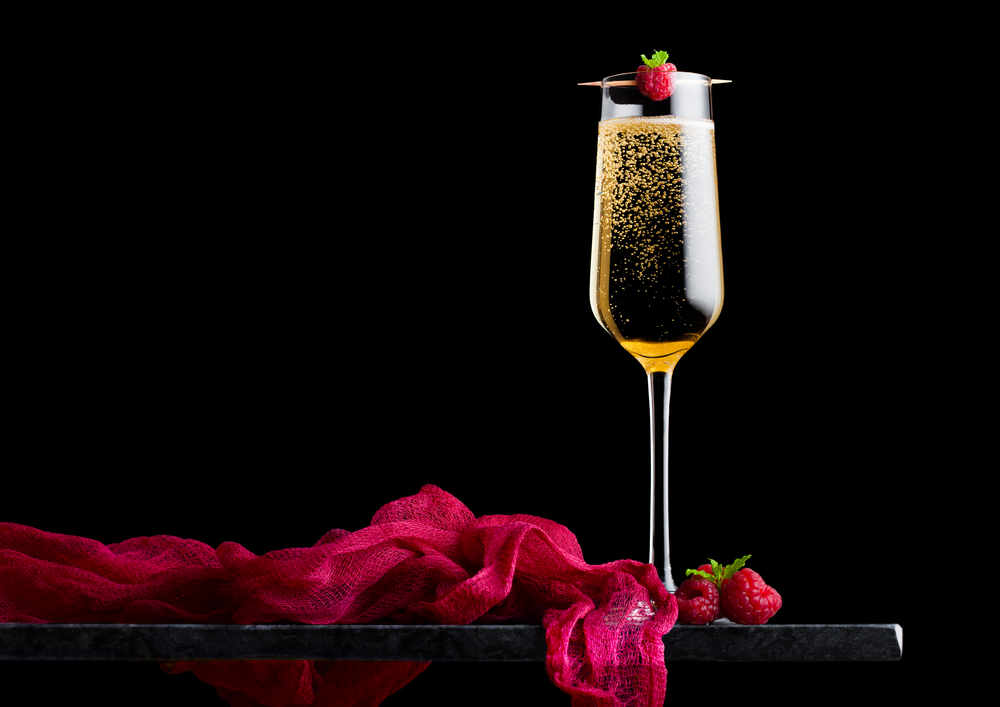 Elegant glass of yellow champagne with rasspbery and fresh berries with mint leaf on stick on black marble board on black.