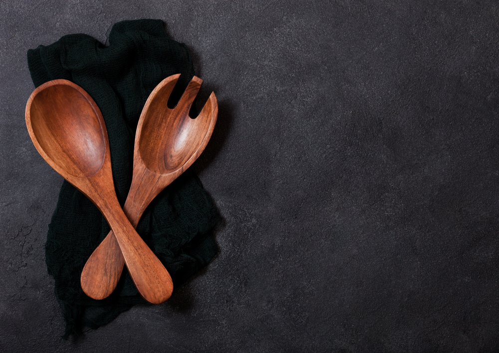 Vintage kitchen wooden utensils over black cloth on stone table background. Top view.